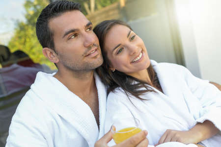 Happy young couple in bathrobes having breakfast outdoorsの写真素材