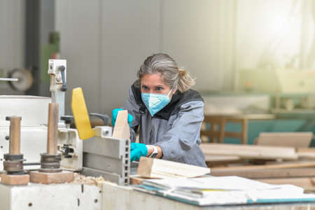 Woman worker operating on a woodworking machinery and wearing protections againt covid-19の写真素材