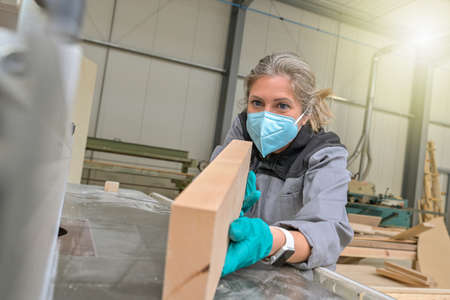 Woman worker operating on a woodworking machinery and wearing protections againt covid-19の写真素材