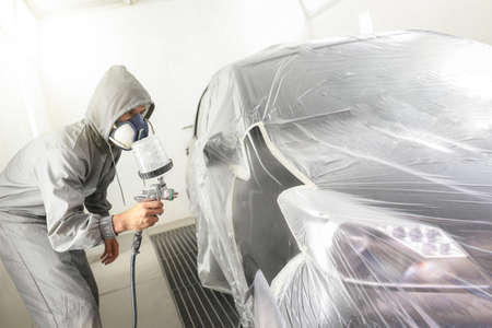 Car body worker paints a car in the paint booth with a spraying paint and a protective maskの写真素材