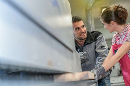 Male worker teaching female apprentice how to operate a machine