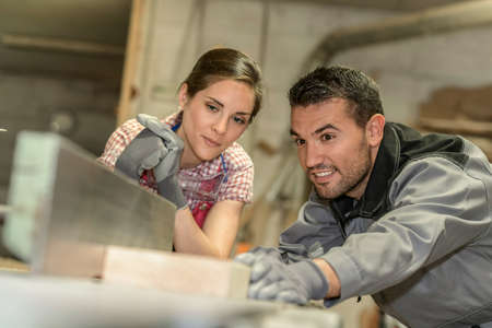 Female trainee and male mentor cutting a piece of wood in workshop