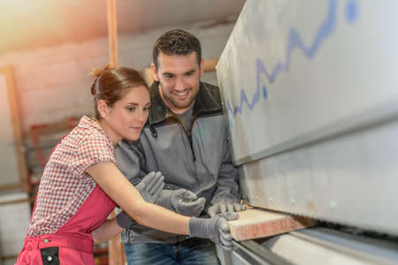 Male worker teaching female apprentice how to operate a machine