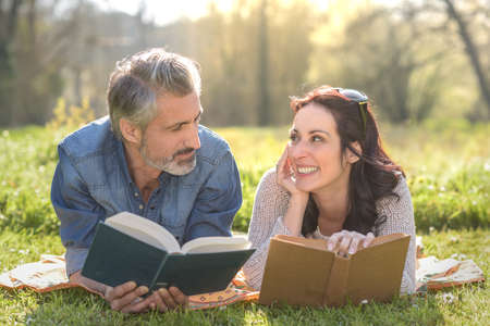 Happy couple reading a book together laying on a blanket outdoorsの写真素材