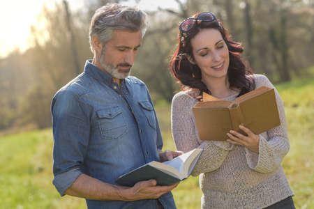 Laughing couple reading a funny book outdoorsの写真素材