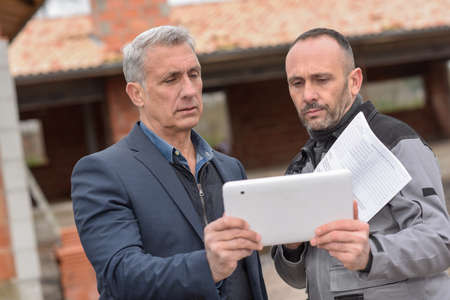 Owner and contractor are reading the notes on the tablet during the construction meetingの写真素材