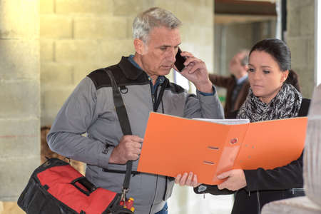 The contractor is on the phone with his supplier while the architect shows him the notesの写真素材