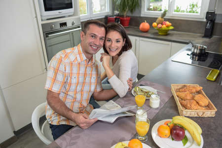 Young couple enjoys their breakfast and reads newspaper in the kitchenの写真素材