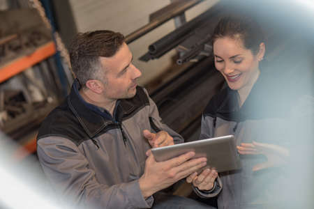 Two workers are checking the tablet while working in a metal warehouseの写真素材