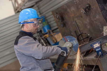 Male worker wearing protective cloths cutting a metal bar with circular sawの写真素材