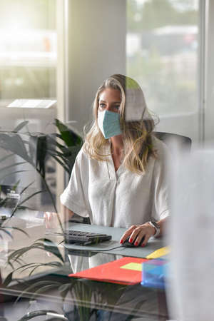 Executive woman working at her desk and wearing a protective mask against covid-19の写真素材