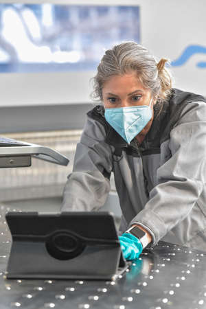 Concentrated female engineer reading her digital tablet in the workshop and wearing a protective mask againt coronavirusの写真素材