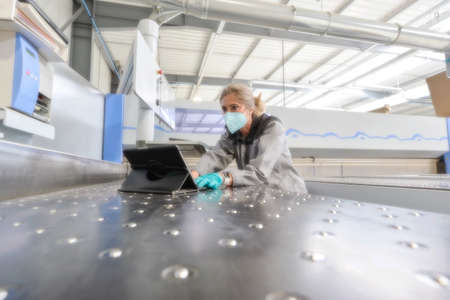 Concentrated female engineer reading her digital tablet in the workshop and wearing a protective mask againt coronavirusの写真素材