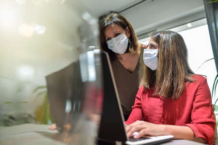Mother and daughter wearing protective mask and attending online video learning lesson during lockdown due to coronavirusの写真素材