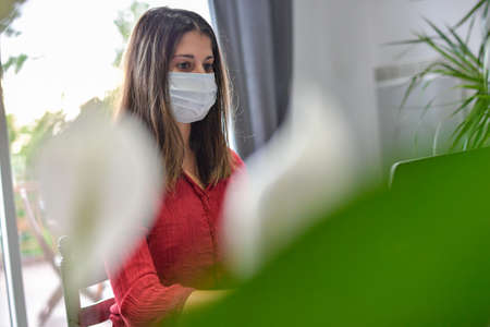Young woman secretary wearing a protective mask while she is working at home and attending at a meeting on her computerの写真素材