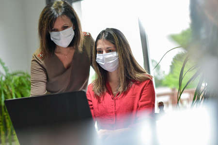 Mother and daughter wearing protective mask and attending online video learning lesson during lockdown due to coronavirusの写真素材