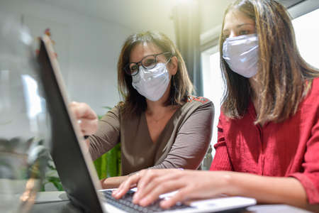 Student and her teacher wearing protective mask and working a lesson on a laptop at home during lockdown due to covid-19の写真素材