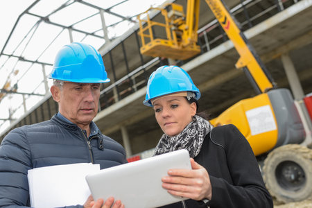 Construction manager and architect reading their notes on a tablet in front of a metallic constructionの写真素材
