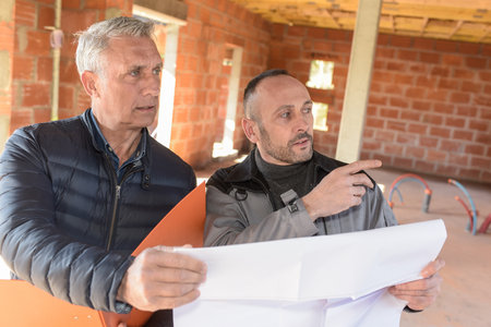 Architect and engineer looking at plans and pointing at something inside construction siteの写真素材