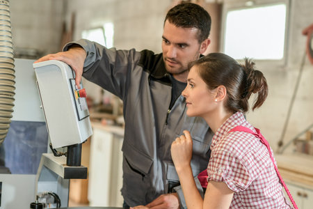Male worker teaching female apprentice how to operate a machineの写真素材
