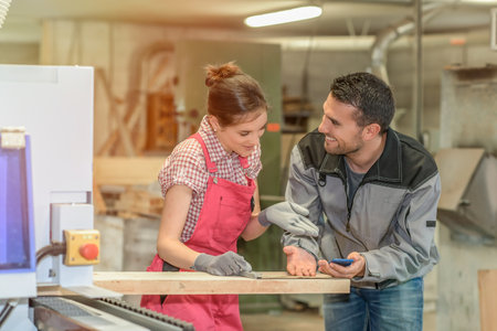 Male worker teaching female apprentice how to operate a machineの写真素材