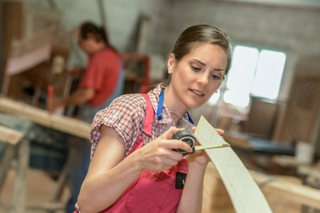 Concentrated female wood worker measuring a piece of woodの写真素材