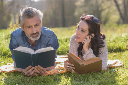 Happy couple reading a book together laying on a blanket outdoorsの写真素材