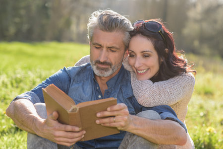 Happy couple reading a book together outdoors laying on a blanketの写真素材