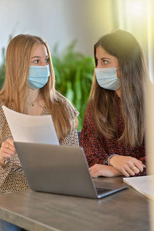 Young female friends wearing a protective mask while they are working at home and attending at a webinar on their laptop during the lockdown due to the coronavirusの写真素材