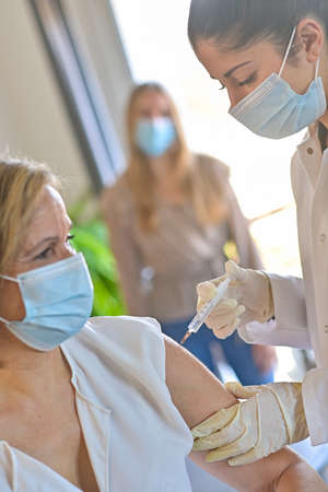 Injection of the vaccine against the covid-19 by a doctor and a nurse in a vaccination centerの写真素材