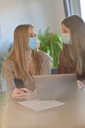 Young female students are working together at home and are wearing protective mask due to the...