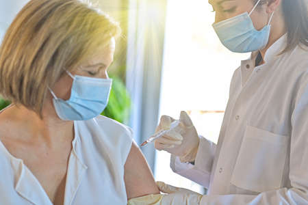 Injection of the vaccine against the covid-19 by a doctor and a nurse in a vaccination centerの写真素材