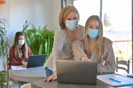 Students and their teacher wearing protective mask and working a lesson on a laptop at home during lockdownの写真素材