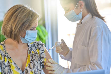 Injection of the vaccine against the virus by a doctor and a nurse in a vaccination centerの写真素材
