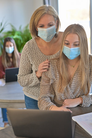 Students and their teacher wearing protective mask and working a lesson on a laptop at home during lockdownの写真素材
