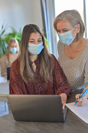 Twin sisters and their mother wearing protective mask and working a lesson on a laptop at home during lockdownの写真素材
