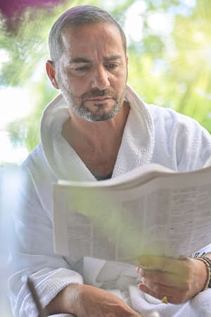Portrait of a man wearing a bathrobe and reading the morning news on a newspaperの写真素材