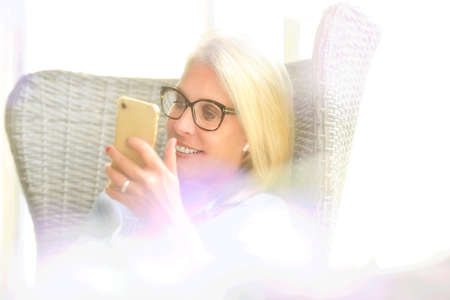 Portrait of a blonde woman on the phone sitting in an armchair on her outdoor patioの写真素材