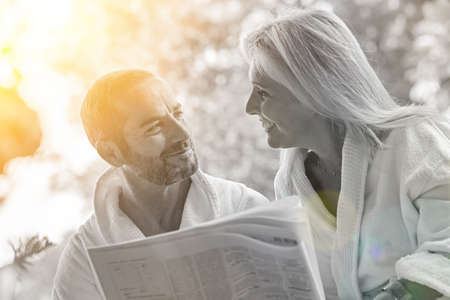 Mature couple wearing bathrobes and reading the morning news on their outdoor terrace during breakfastの写真素材