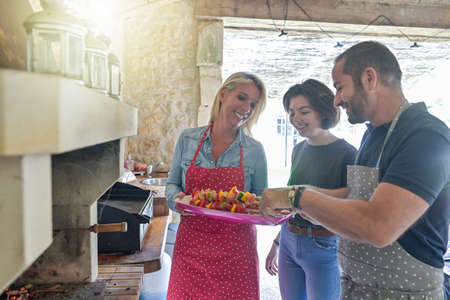Happy family preparing meal together with beef skewers cooking on the barbecue in the chimneyの写真素材