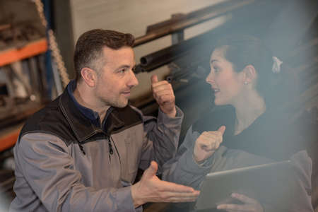 Two workers are checking a technical solution on the tablet while working in a metal warehouseの写真素材