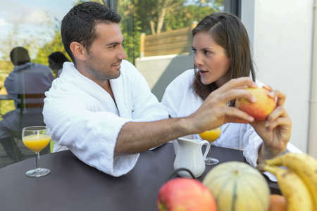 Happy young couple in bathrobes having breakfast outdoorsの写真素材