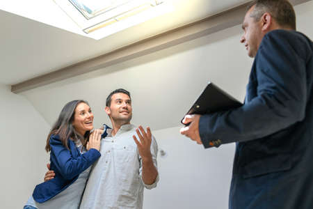 Happy couple visiting a flat with a roof windows in an attic roomの写真素材