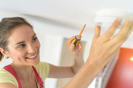 Young woman is fitting a fire alarm in the ceilingの写真素材