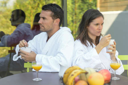 Happy young couple in bathrobes having breakfast outdoorsの写真素材