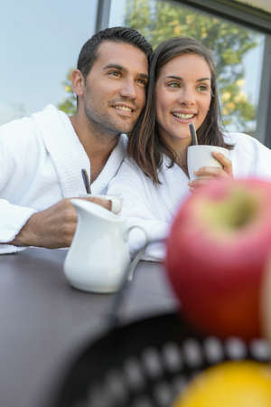 Happy young couple in bathrobes having breakfast outdoorsの写真素材