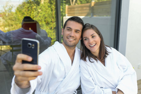 Happy young couple in bathrobes doing a selfie with a phone outdoorsの写真素材