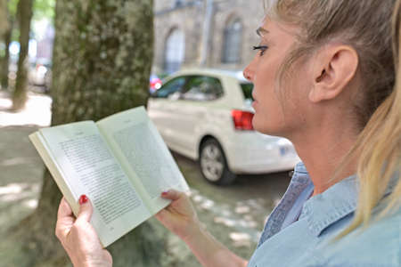 Woman doing a break outdoors, setting on a bench and reading a bookの写真素材