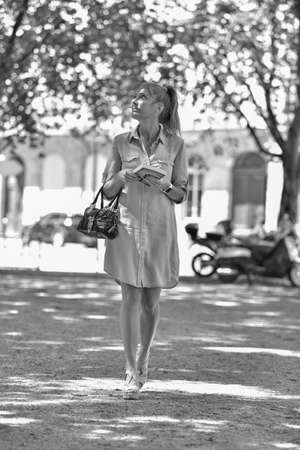Fashionable woman walking in street wearing a handbag and looking at her bookの写真素材