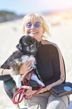 Retired mature blonde woman walking her dog alone on the beachの写真素材